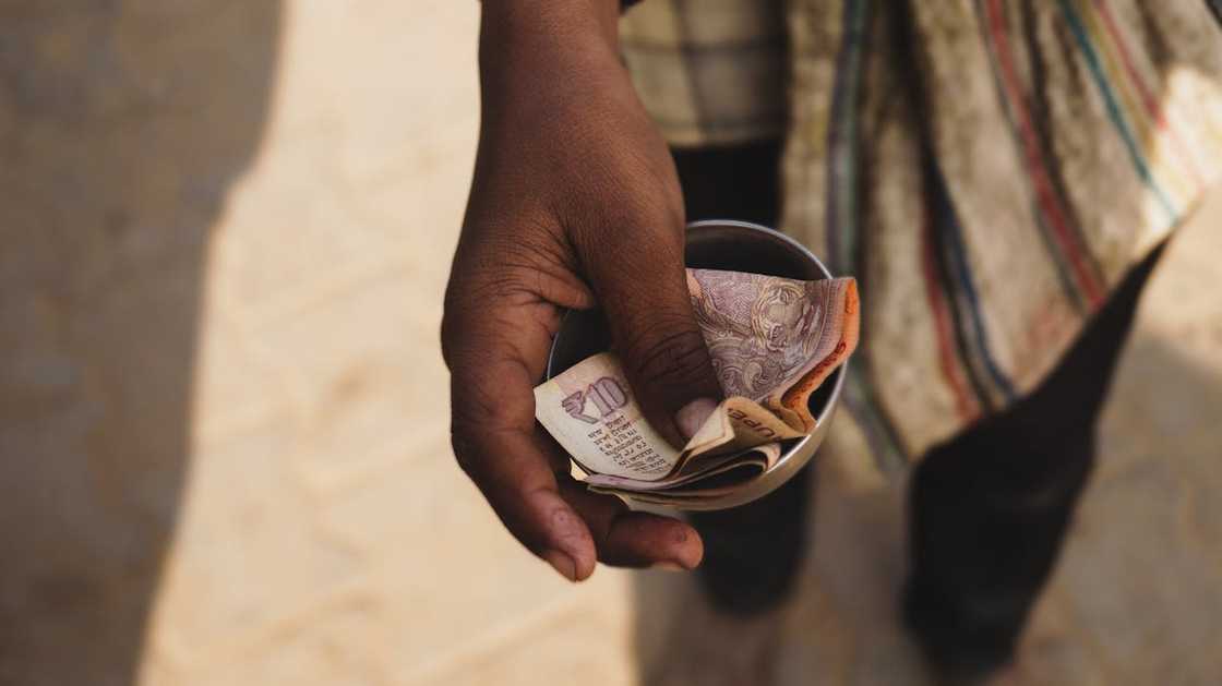 A hand holding a small bowl with folded paper money. A hand holding a small bowl with folded paper money.
