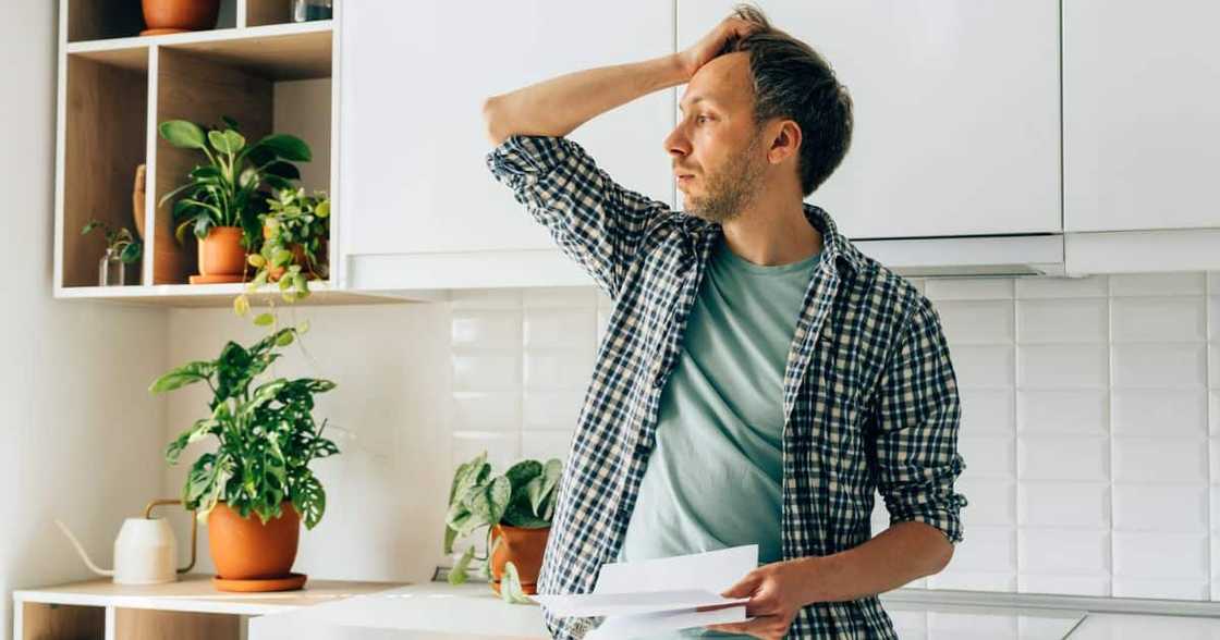 Man stands in kitchen looking stressed.