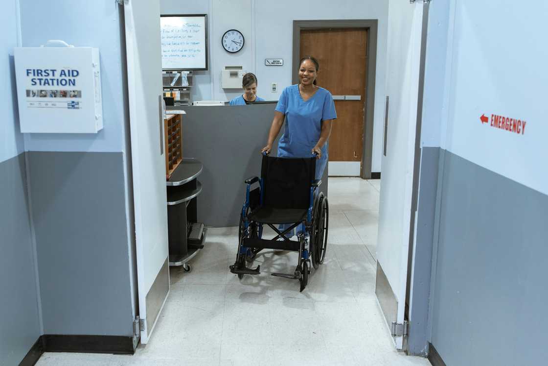 A female healthcare provider in blue scrubs is pushing a wheelchair