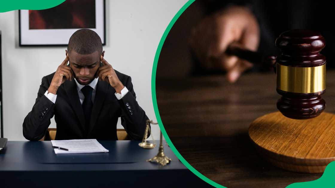 A lawyer in a black suit is reading a document in his office and a hand is holding a brown wooden gavel on a brown table