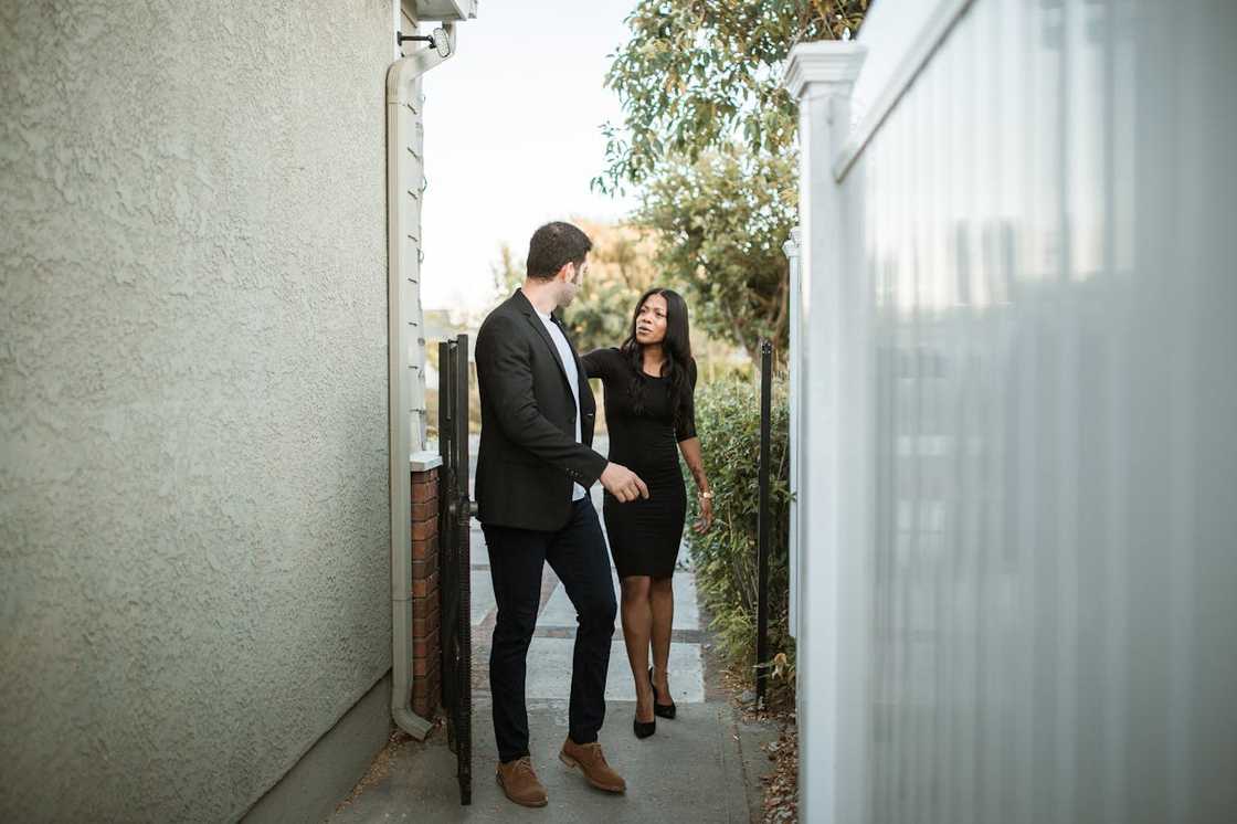 A man and a woman walk through a narrow outdoor passage while talking. A man and a woman walk through a narrow outdoor passage while talking.