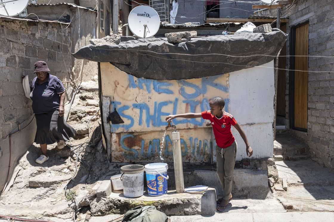 A child fills up water buckets as a resident walks past in Alexandra near Johannesburg on November 28, 2024