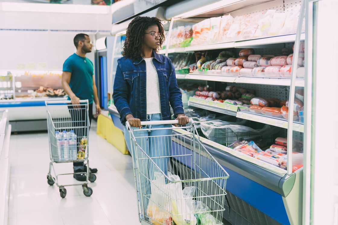 Two people shop with carts in a brightly lit grocery store.