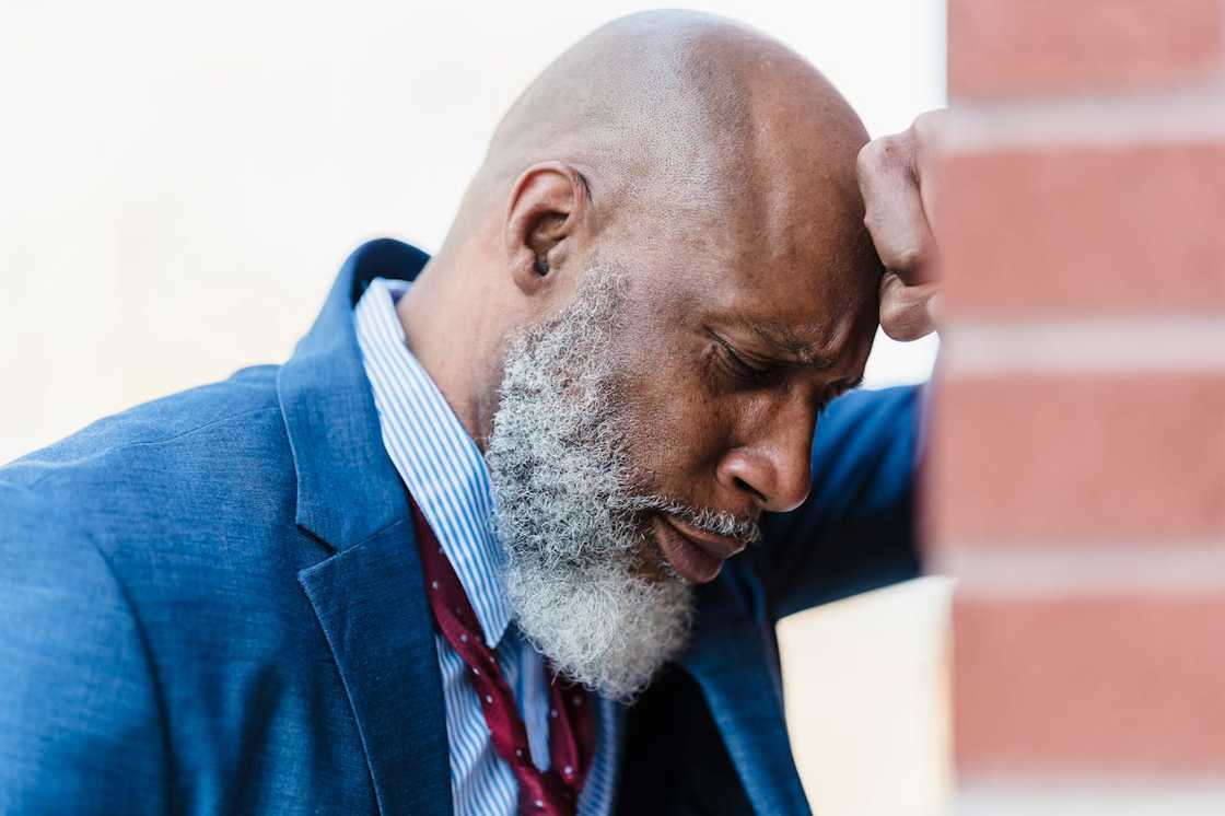 An older man leans his head against a brick wall, appearing stressed. An older man leans his head against a brick wall, appearing stressed.