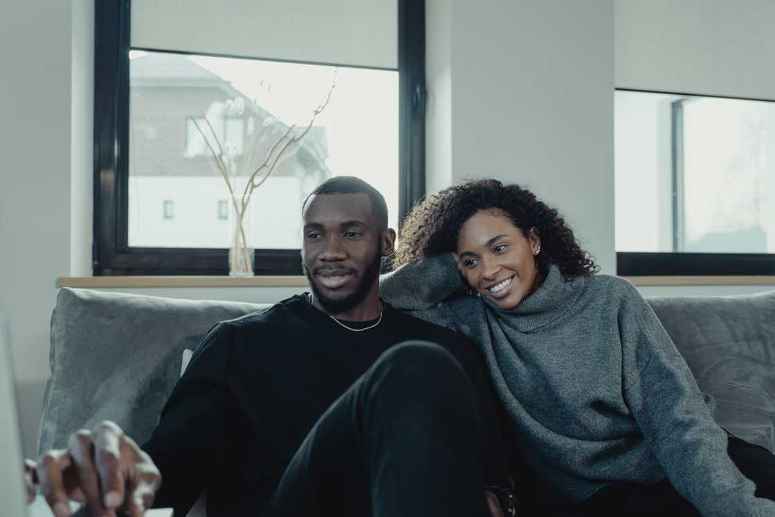 A couple sits close together on a sofa, smiling and relaxed at home.