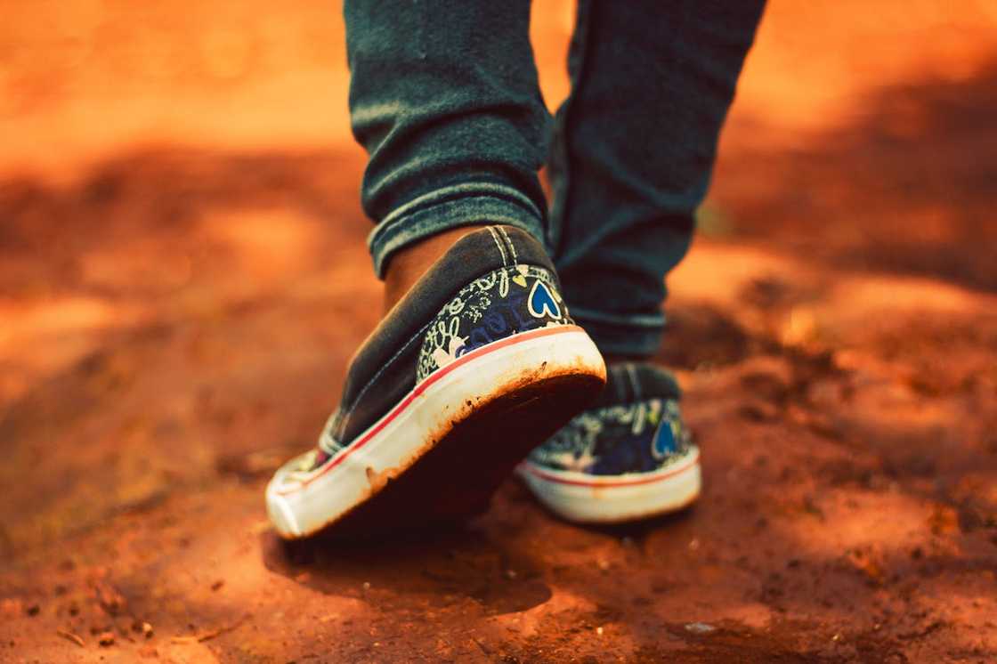 A person in worn trainers steps forward on a dusty ground.