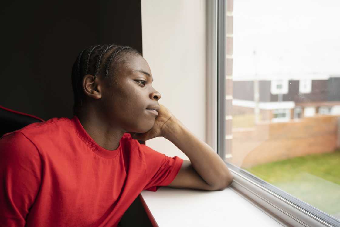 A young boy looking out the window as he ponders