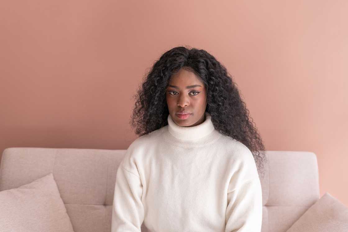 A young woman sitting on a sofa against a pink background A young woman sitting on a sofa against a pink background