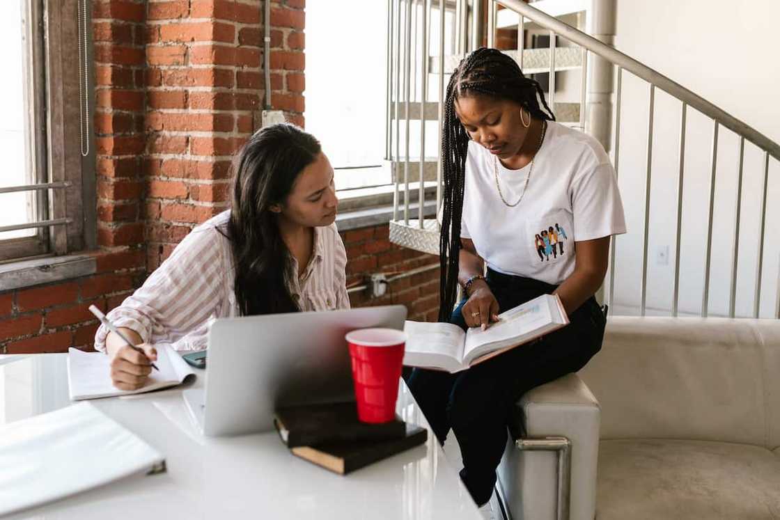 Two ladies studying together in a brick-walled building