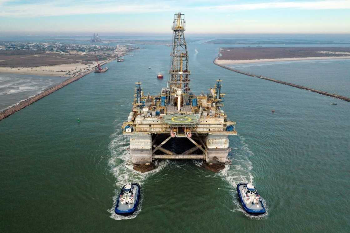 In this aerial image from a drone, tug boats tow the semi-submersible drilling platform Noble Danny Adkins through the Port Aransas Channel into the Gulf of Mexico