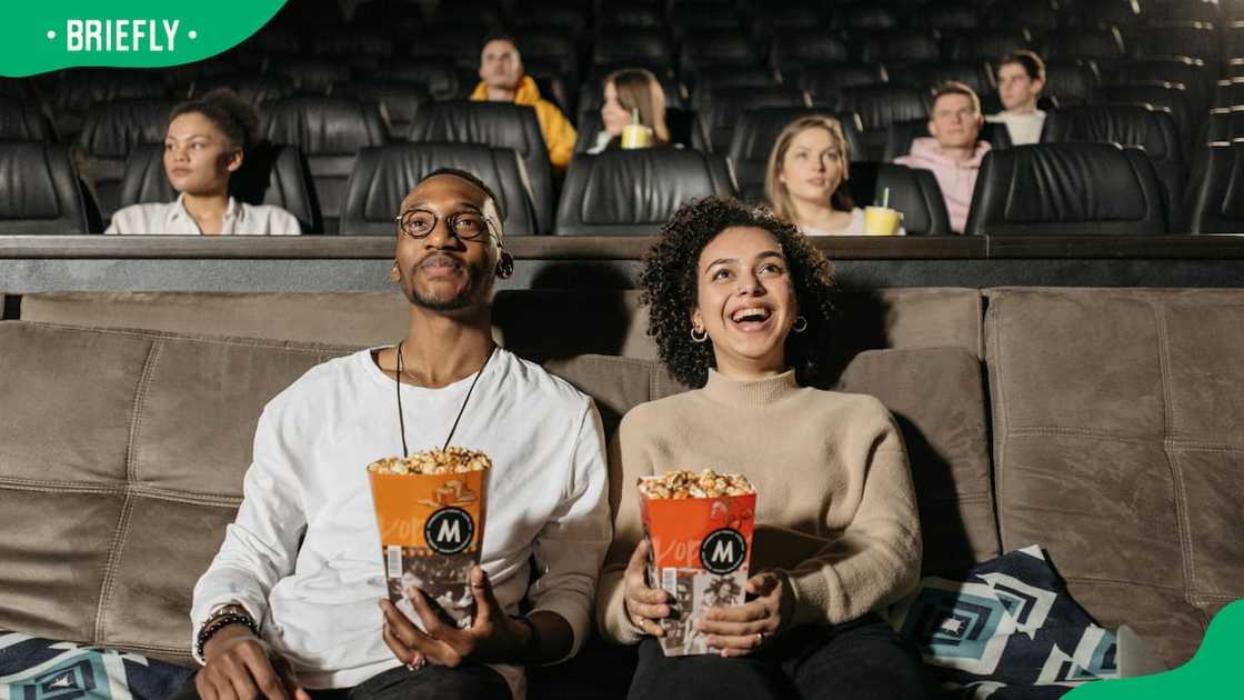 A couple holding popcorns while watching a movie. A couple holding popcorns while watching a movie.