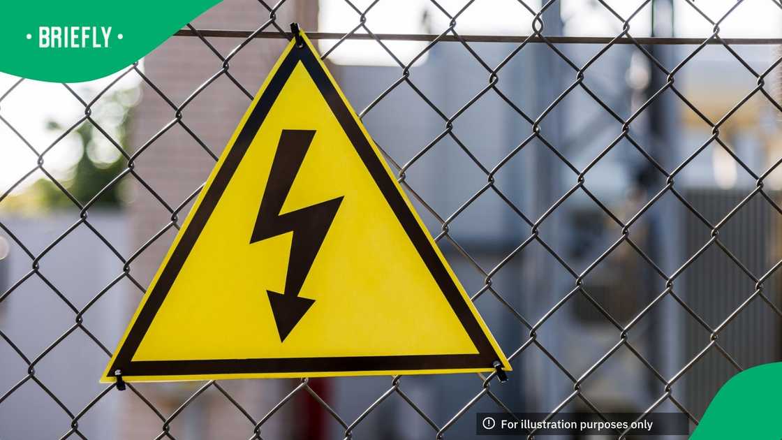 Close-up of a yellow high voltage caution sign hanging on chain fence. Shallow depth of field Close-up of a yellow high voltage caution sign hanging on chain fence. Shallow depth of field
