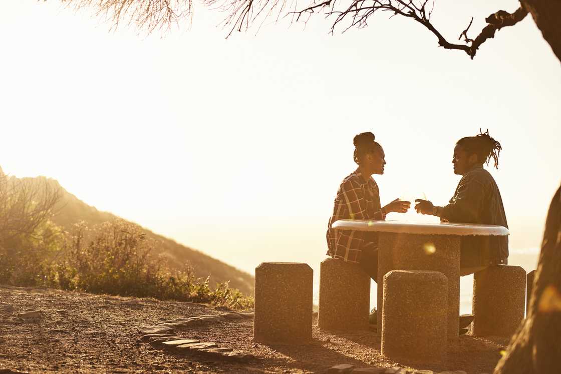 Two people sit at a stone picnic table during sunset. Two people sit at a stone picnic table during sunset.
