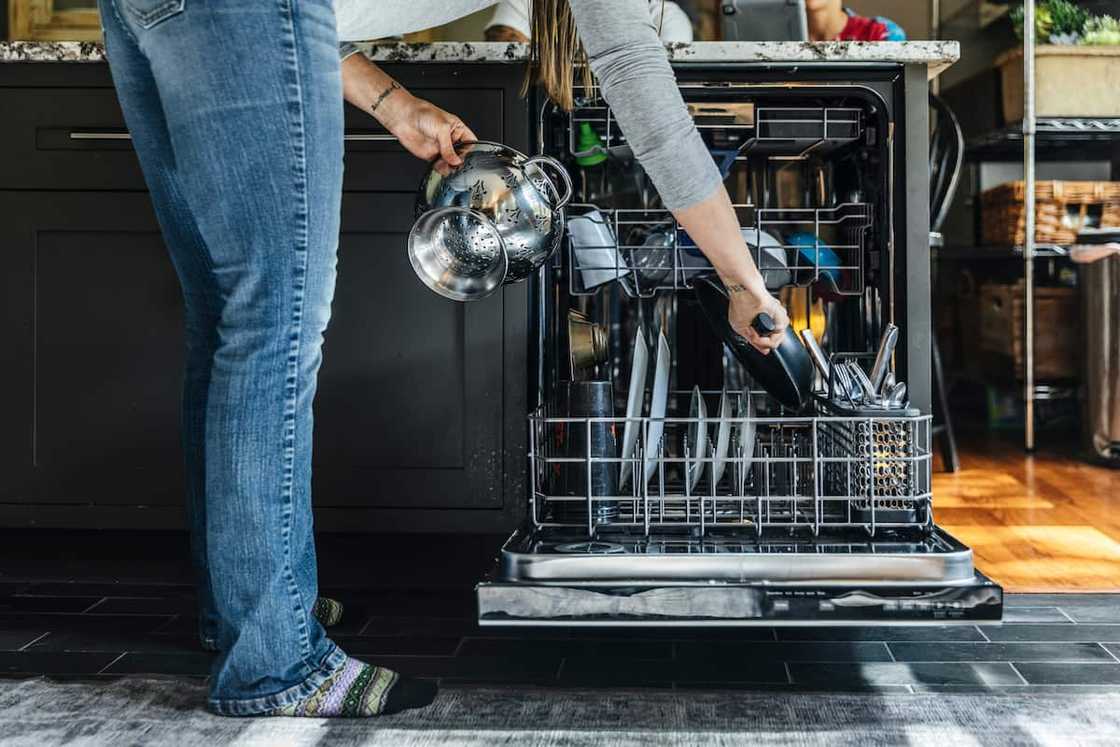 Woman arranging utensils in dishwasher at home Woman arranging utensils in dishwasher at home