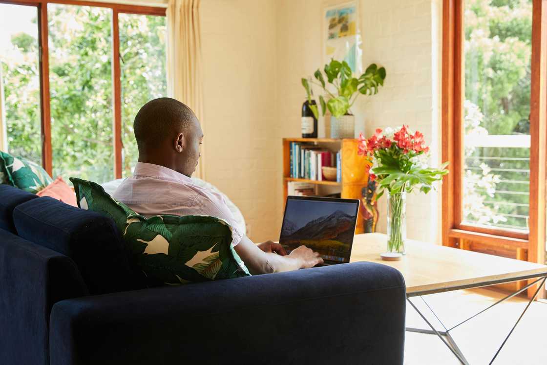 A man in a white shirt is using a laptop while sitting on a navy blue couch