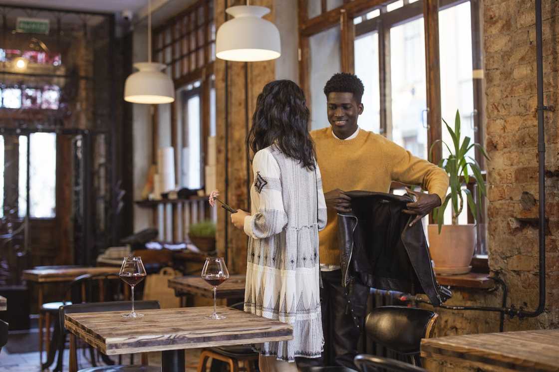 A man helps a woman with her jacket in a restaurant.