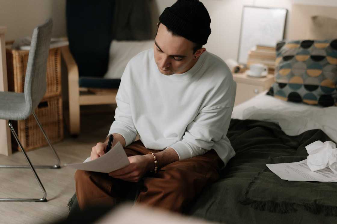 A man sits on a bed while reading paperwork.