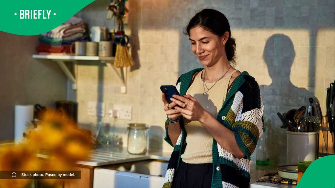 A woman in a kitchen smiling at her phone.