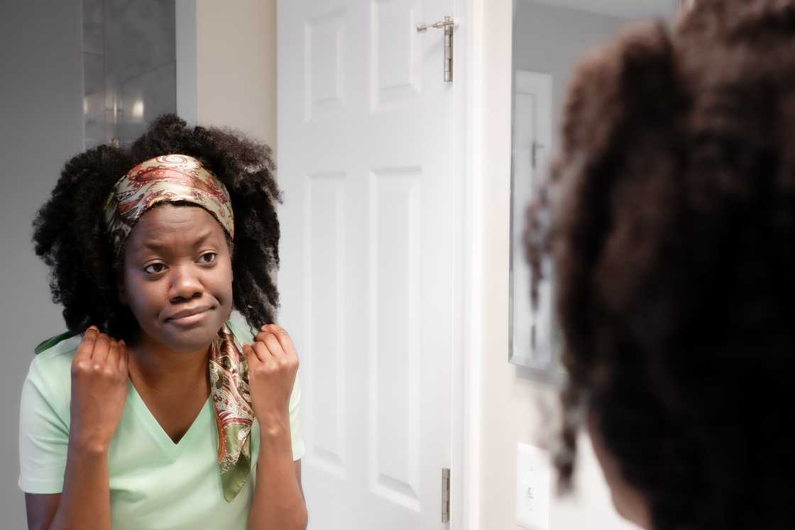 A woman touches her hair, pausing to look at her reflection.