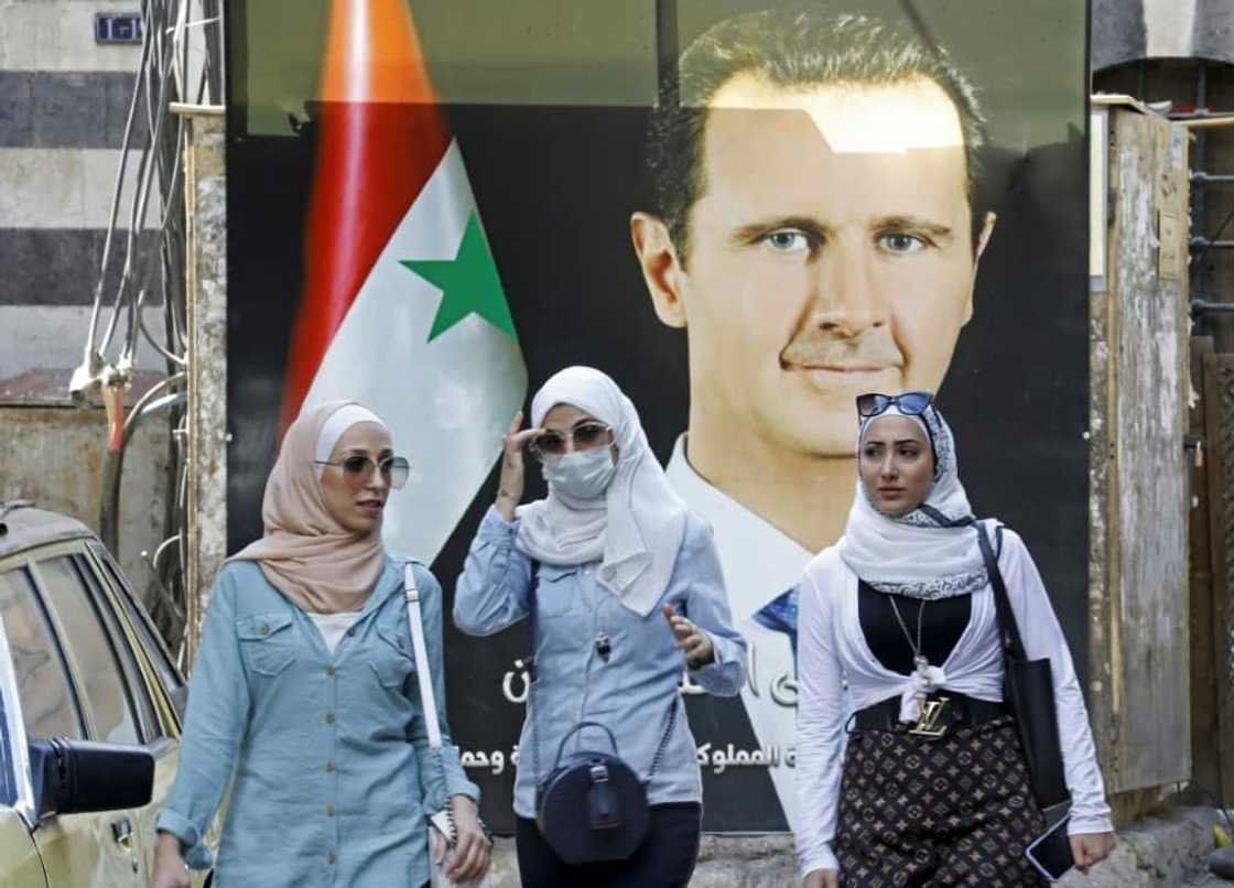 Syrians walk in front of a poster of President Bashar al-Assad near the Grand Umayyad Mosque in Damascus on September 23, 2021 Syrians walk in front of a poster of President Bashar al-Assad near the Grand Umayyad Mosque in Damascus on September 23, 2021