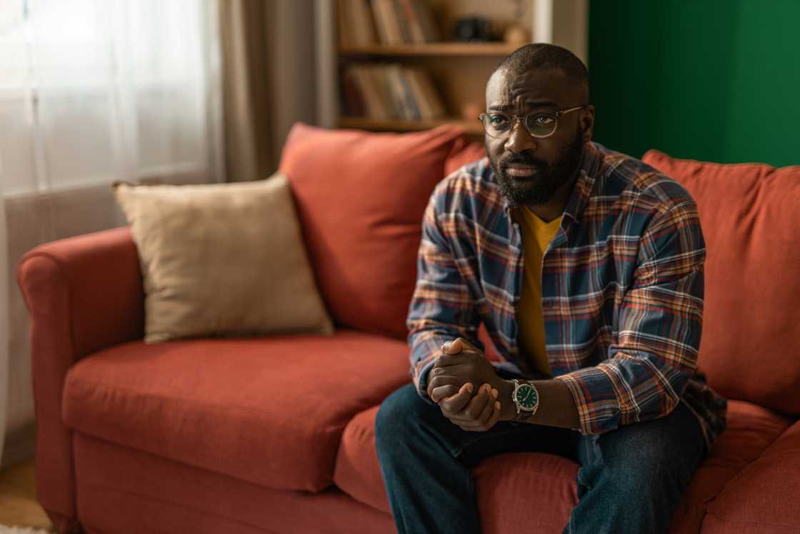 A young adult man sitting on a sofa feeling sad and contemplating A young adult man sitting on a sofa feeling sad and contemplating