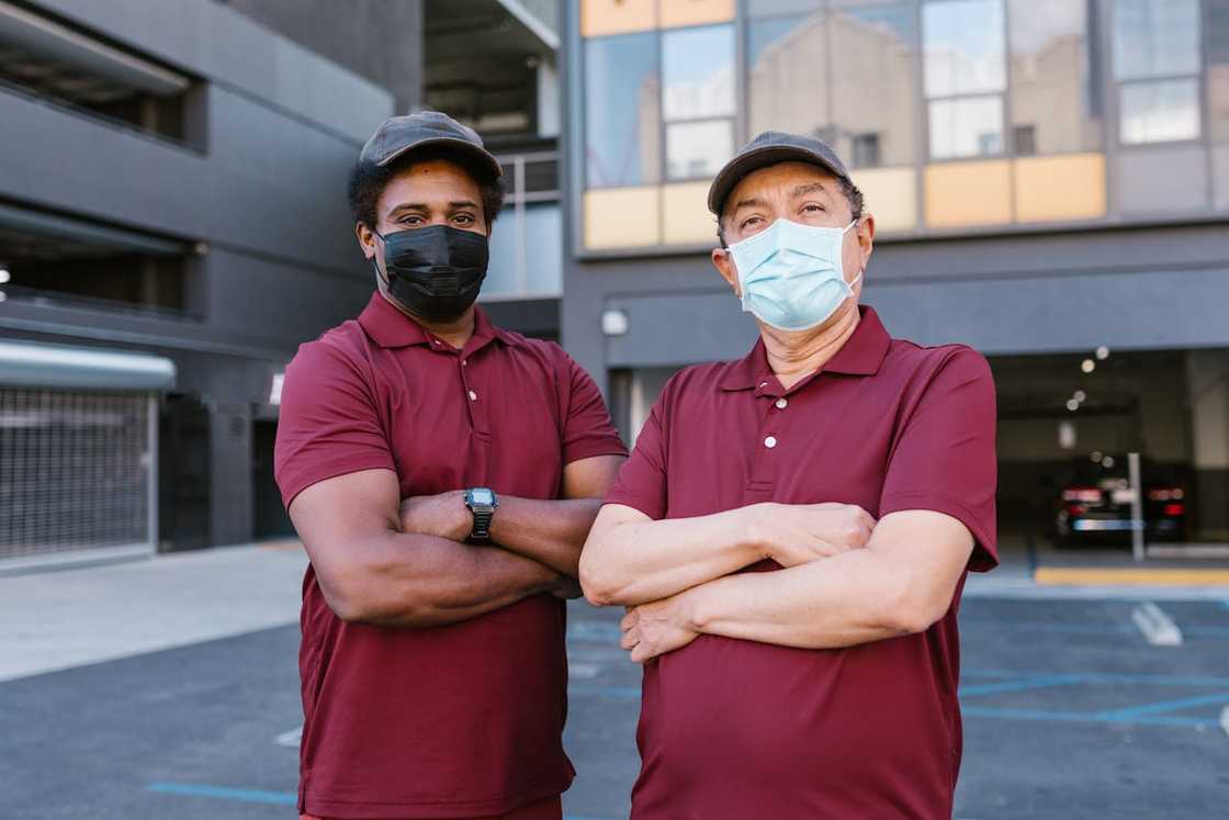 Two delivery workers standing outside a building wearing masks. Two delivery workers standing outside a building wearing masks.