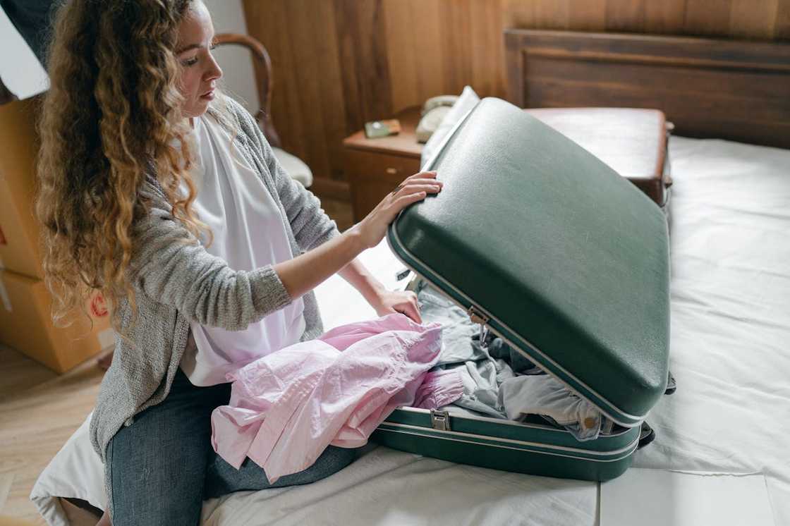 A woman packs clothes into a suitcase on a bed.