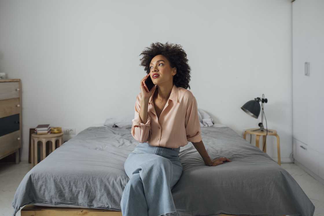 A serious woman sitting on a bed and speaking on the phone