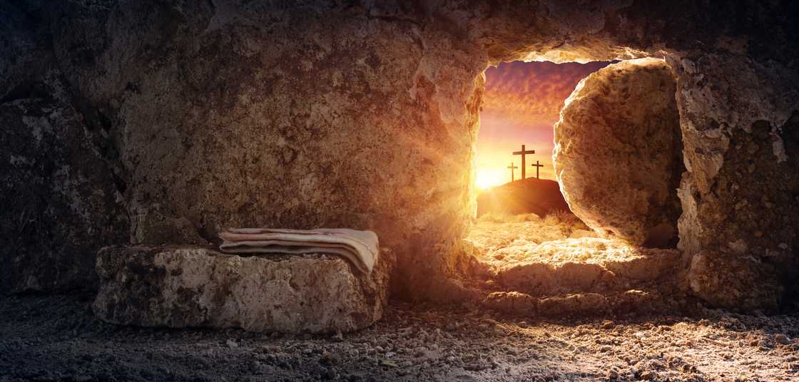 Empty tomb of Jesus at sunrise with crosses in background.