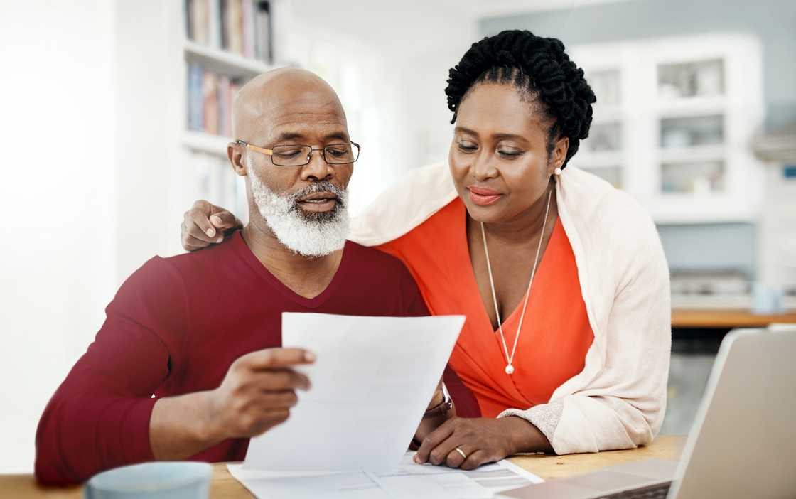 Two adults sit in a home setting, reviewing a piece of paper together. Two adults sit in a home setting, reviewing a piece of paper together.