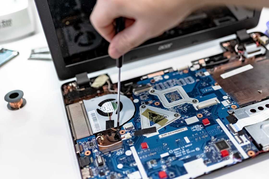 Hand using a screwdriver to repair an open laptop motherboard. Hand using a screwdriver to repair an open laptop motherboard.