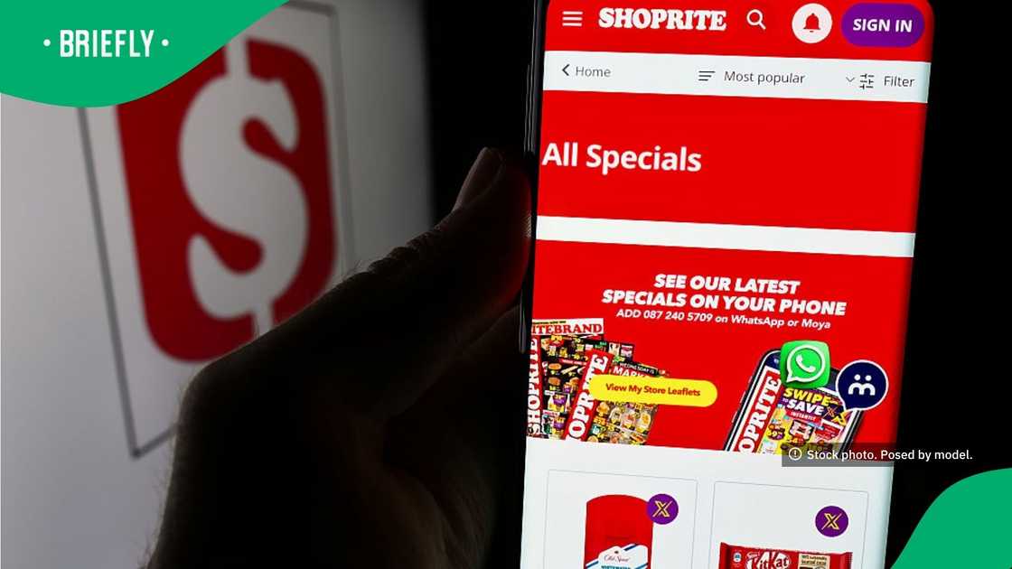 A hand held a smartphone displaying the specials page of the Shoprite mobile app in front of a blurry screen showing the company's red logo A hand held a smartphone displaying the specials page of the Shoprite mobile app in front of a blurry screen showing the company's red logo