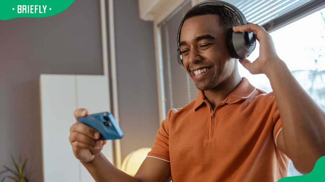 A man wearing headphones while holding a phone in his hand A man wearing headphones while holding a phone in his hand