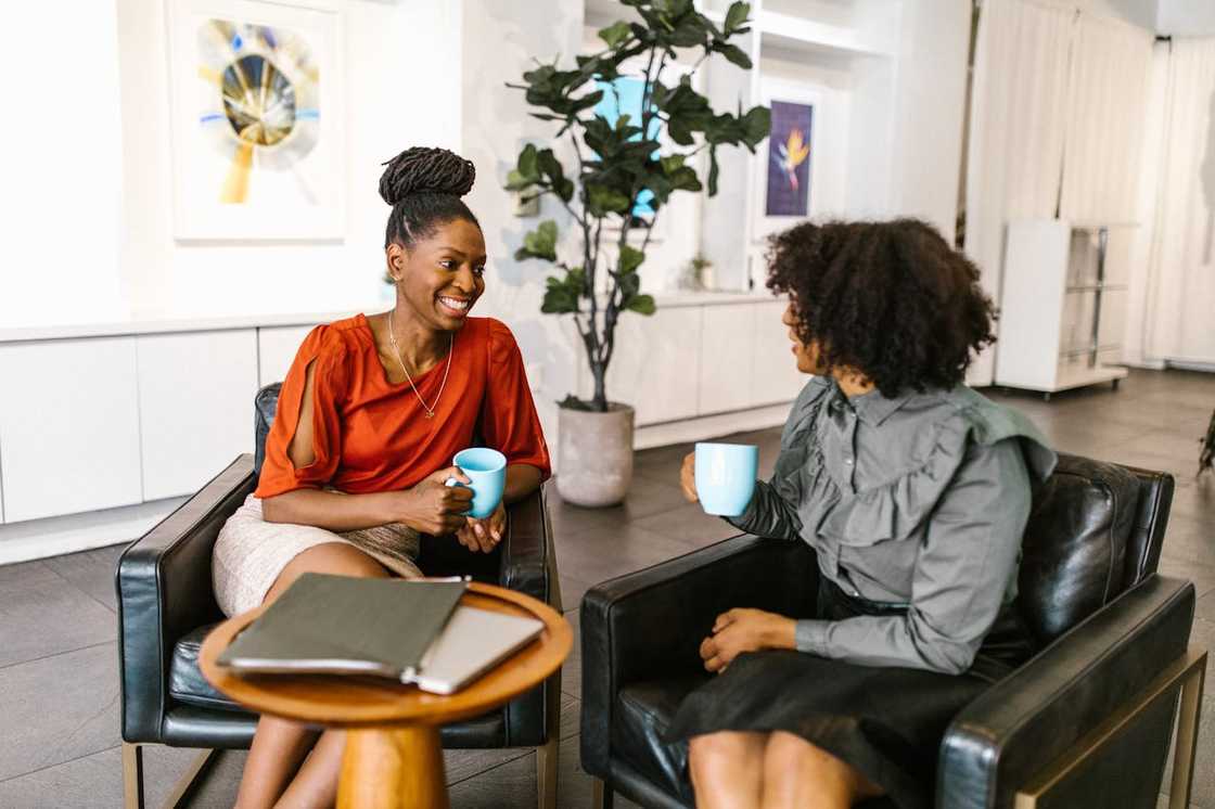 Two women smiling and chatting over coffee in a relaxed setting. Two women smiling and chatting over coffee in a relaxed setting.