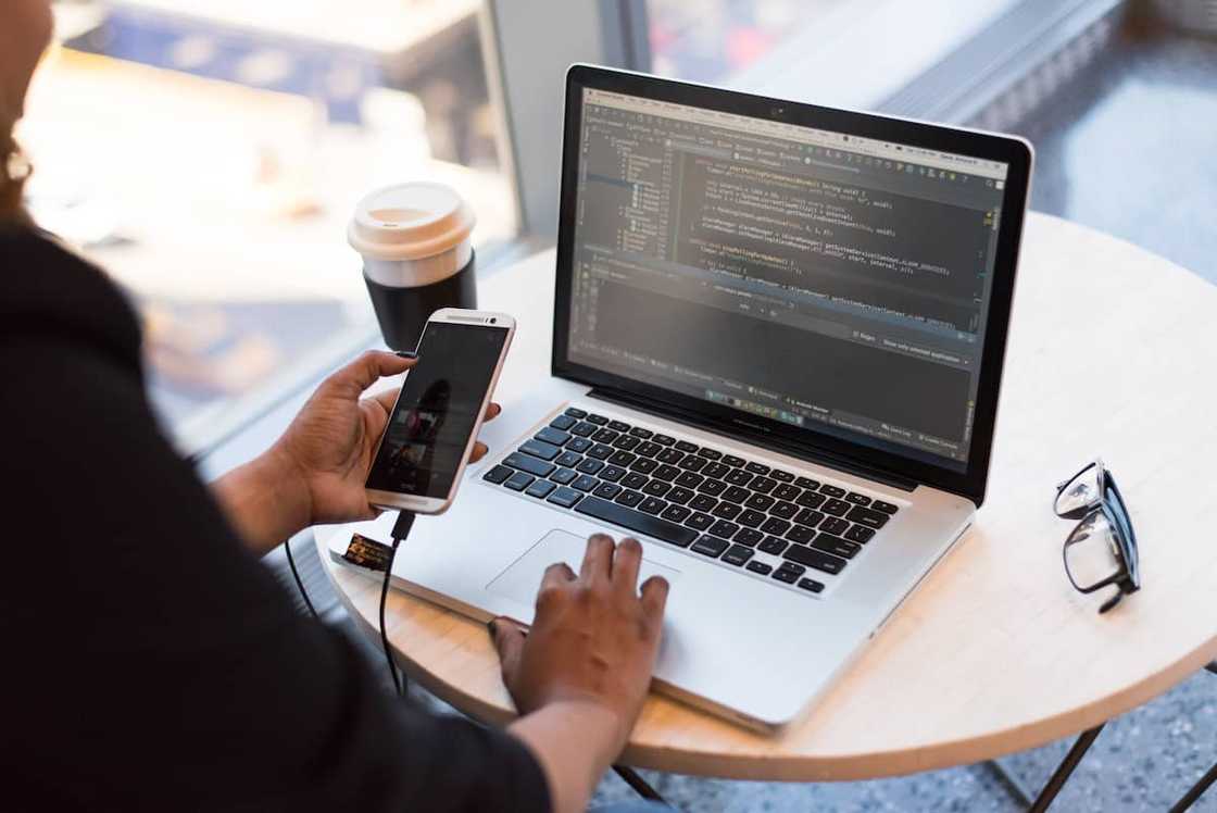 A person holding a smartphone while using a laptop