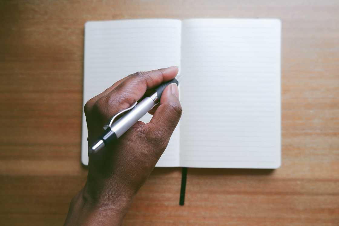 Hand holds pen above a blank notebook on a wooden surface.