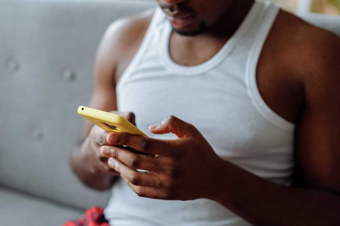 A man sits on a sofa looking down at a phone in his hands.