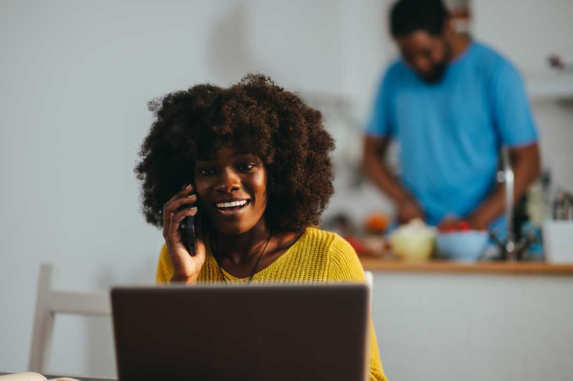 A woman on a call with her partner in the background.