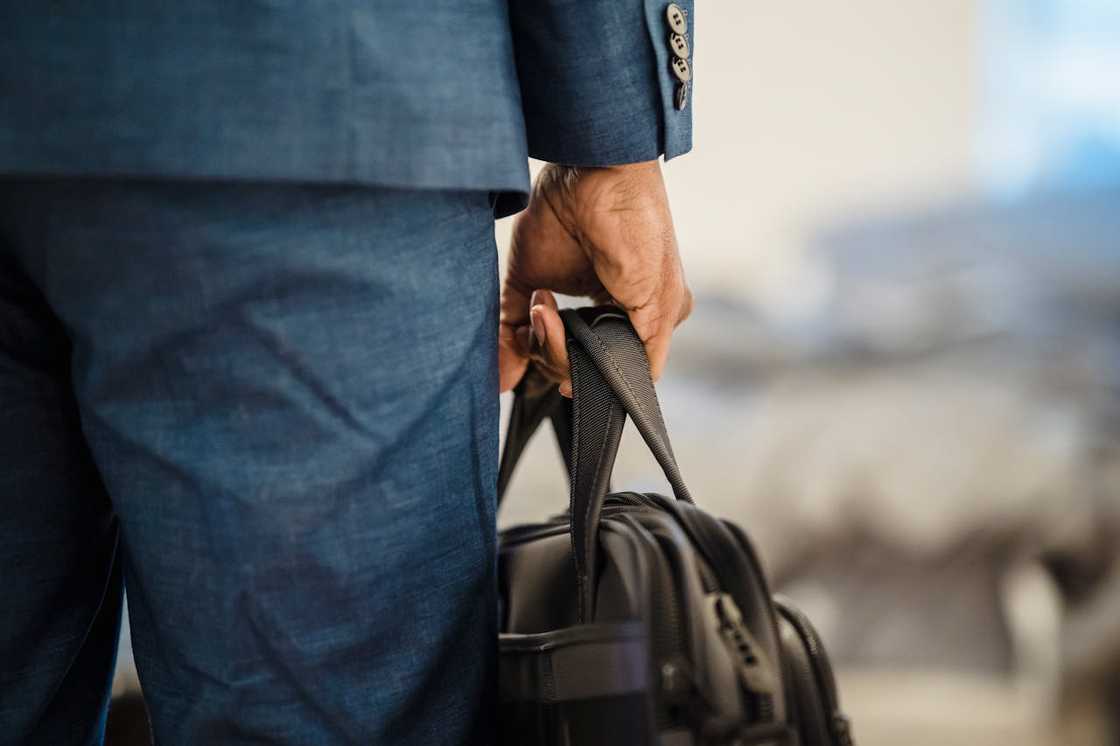 Man in a suit holding a black bag by his side.