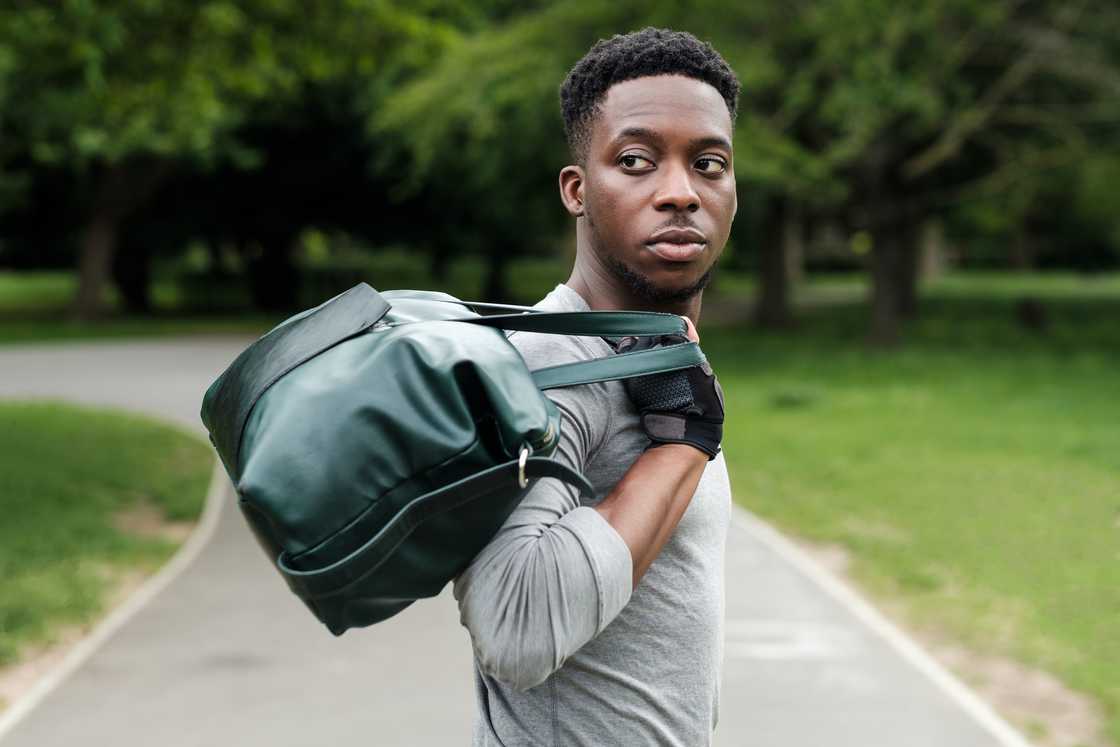 A young man walks on a paved path carrying a duffel bag in a park setting. A young man walks on a paved path carrying a duffel bag in a park setting.