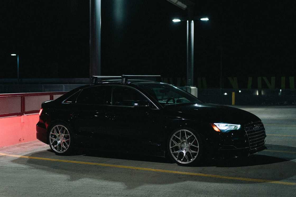 A black car is parked in a dimly lit parking area at night. A black car is parked in a dimly lit parking area at night.