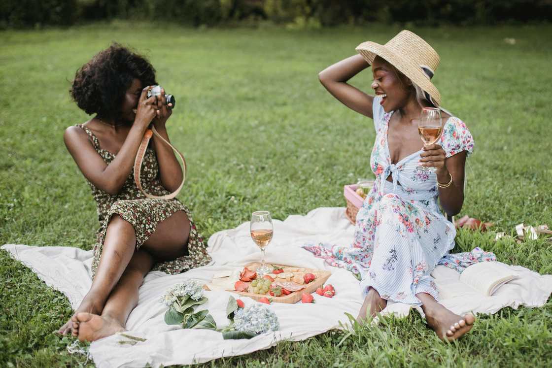 A woman taking a picture of another happy woman during a picnic date A woman taking a picture of another happy woman during a picnic date