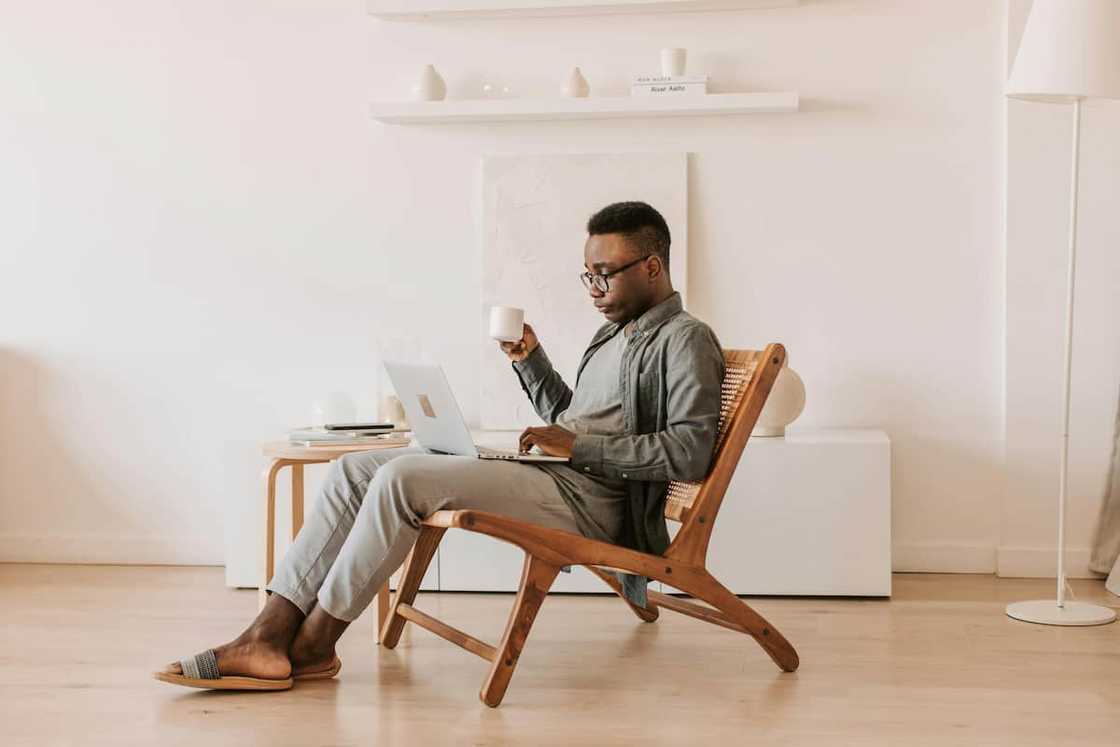 A man in a grey outfit sitting with a laptop on his lap A man in a grey outfit sitting with a laptop on his lap