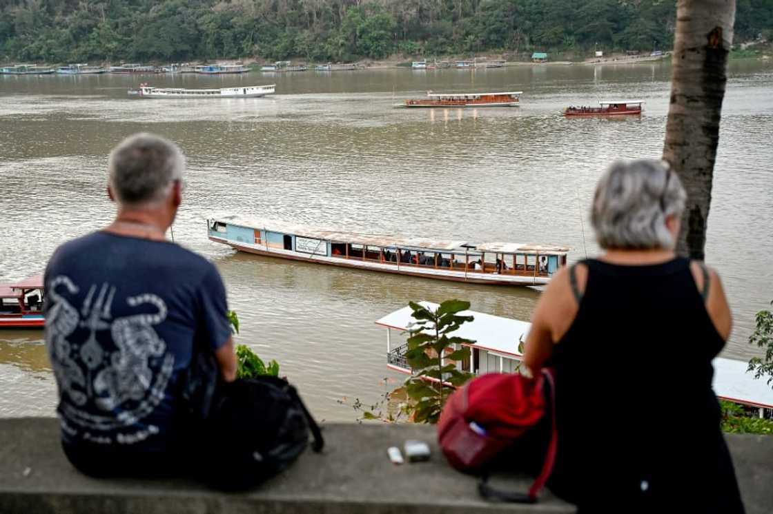 Tourists watch boats cruising on the Mekong river in Luang Prabang