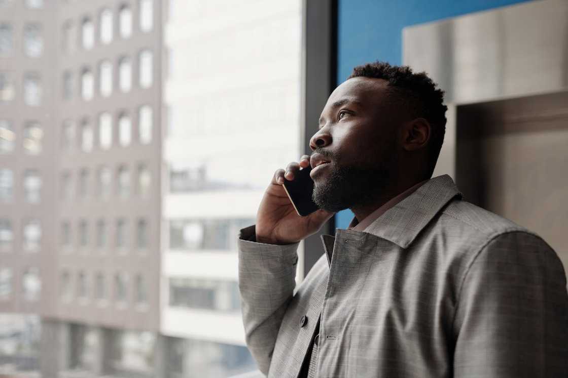 A man stands by a window talking on his phone and looking outside.