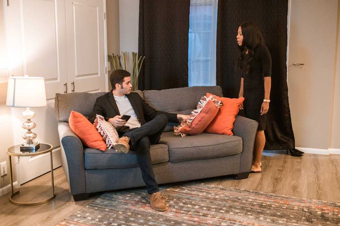 A woman confronts a man sitting on a sofa in a tense living room scene. A woman confronts a man sitting on a sofa in a tense living room scene.