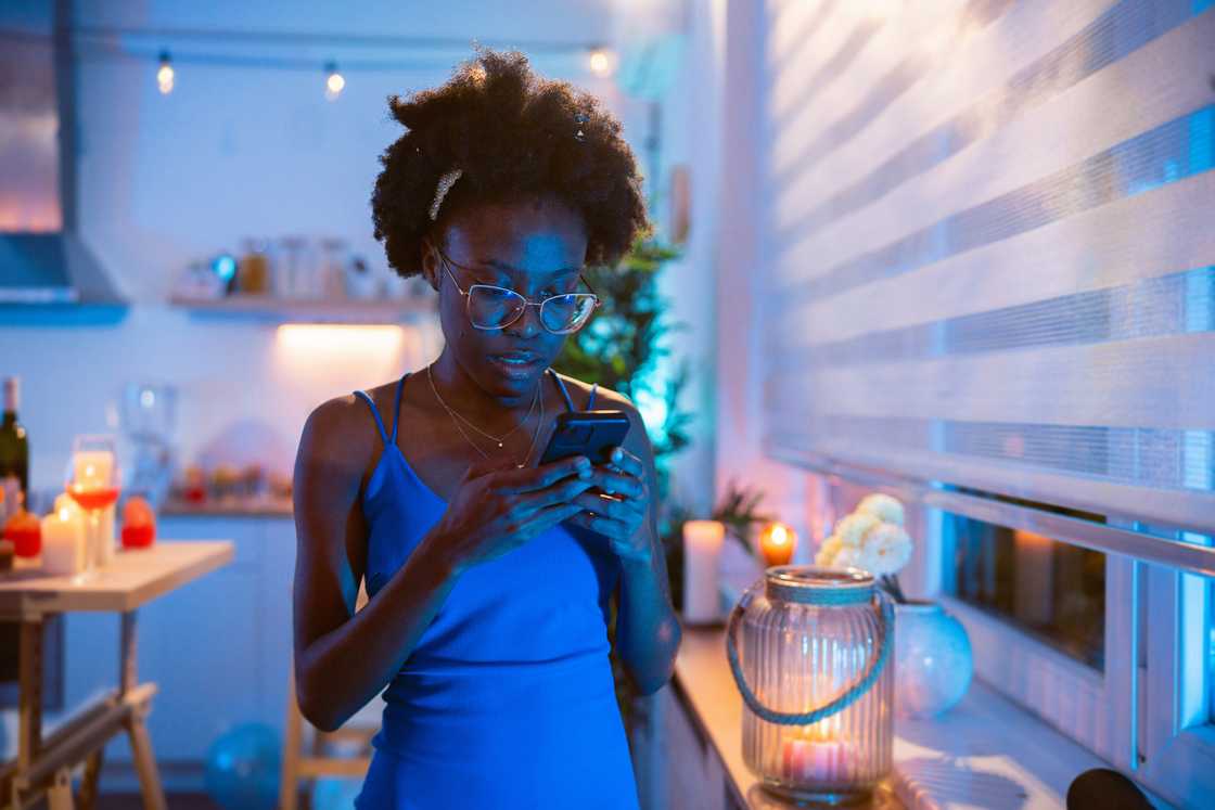 Person in blue dress looks at phone in a warmly lit room. Person in blue dress looks at phone in a warmly lit room.