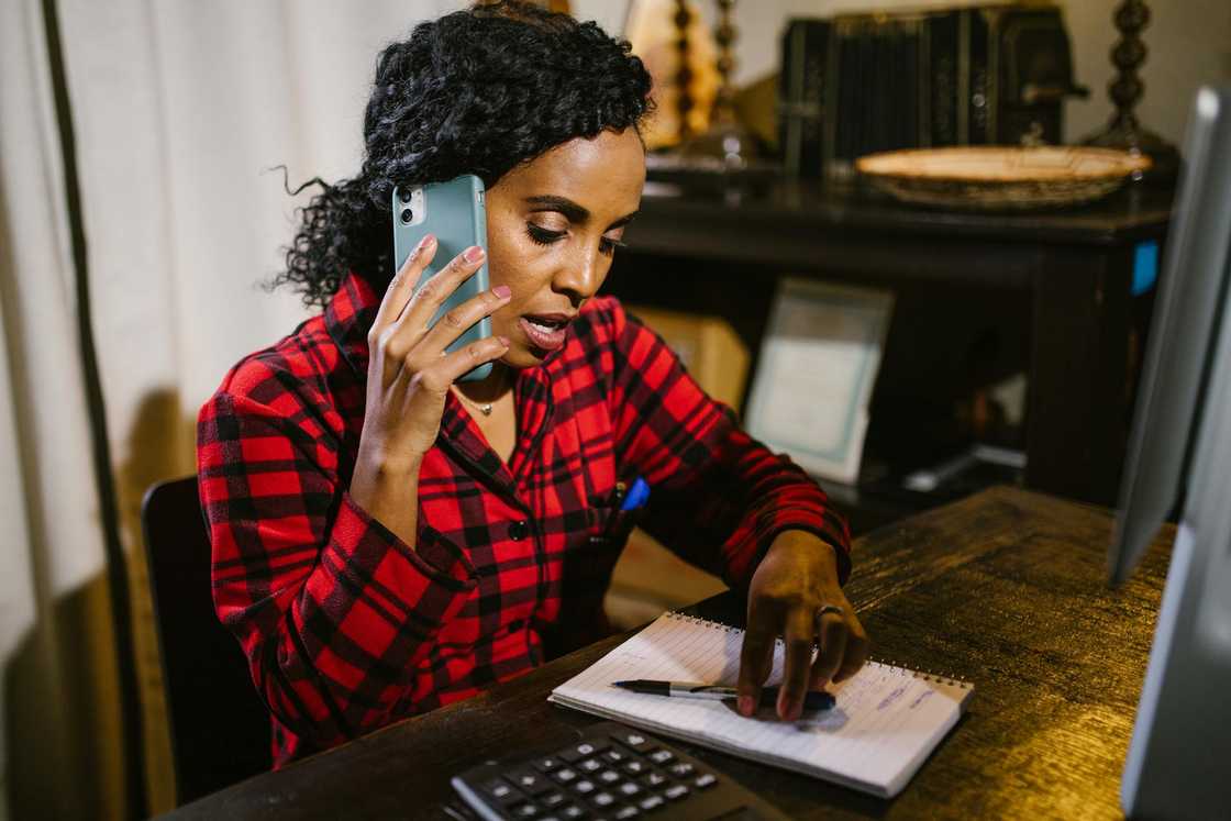 A woman talks on the phone while writing in a notebook. A woman talks on the phone while writing in a notebook.