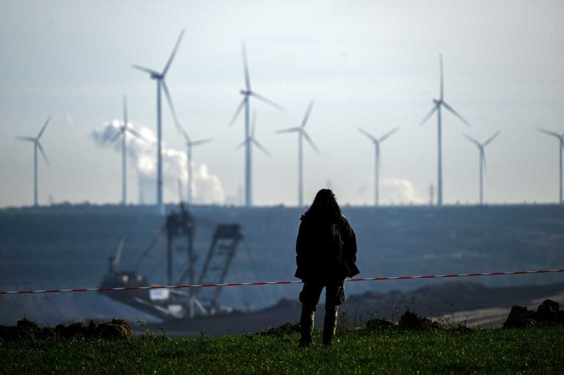 A woman stands on the edge of Germany's Garzweiler lignite open cast mine on November 12, 2022, with wind turbines in the background