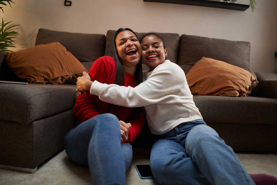 Two people sit on the floor hugging and smiling.
